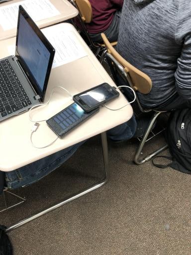 学生用手机上的灯给便携式太阳能电池充电，这样他就可以给手机充电了